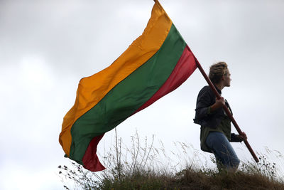 Low angle view of woman holding flag against sky