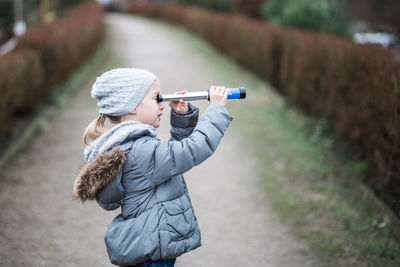 Side view of girl looking through telescope while standing on footpath