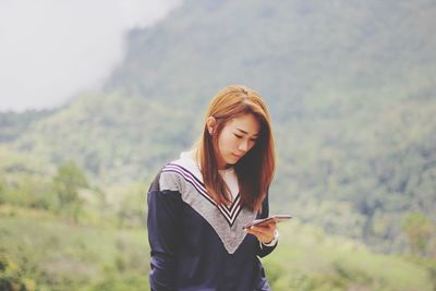 Young woman using mobile phone while standing on mountain