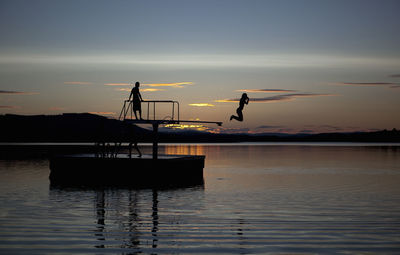 Silhouette woman jumping in lake from diving platform