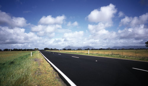Empty road on grassy field against sky