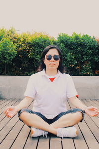 Young man sitting on sunglasses against plants