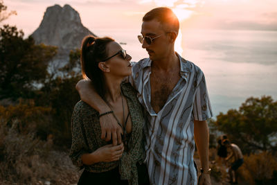 Young couple standing on rock against sky