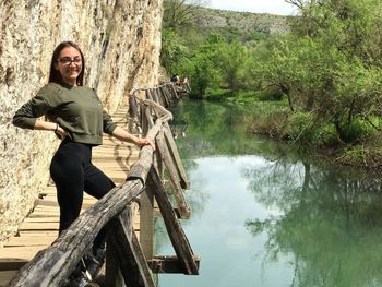 Portrait of smiling woman standing by lake against trees