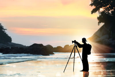 Silhouette man photographing at beach against sky during sunset