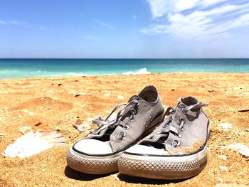 Low section of shoes on beach against sky