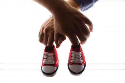 Cropped hands of couple holing canvas shoes against white background