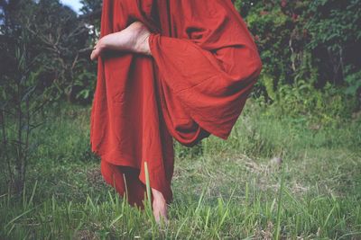 Low section of woman practicing yoga while standing on grassy field