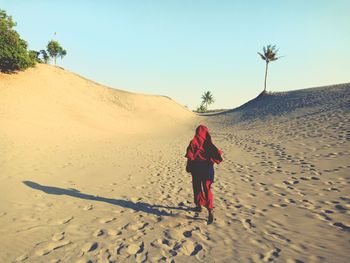 Rear view of woman walking on sand at desert