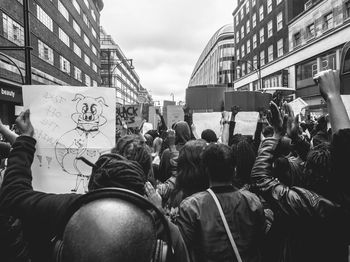 Rear view of crowd protesting on street amidst buildings