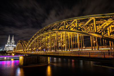 Illuminated bridge over river against sky at night