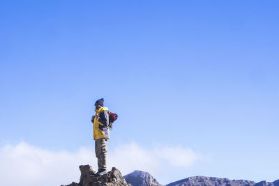 Low angle view of mature man standing on mountain against blue sky