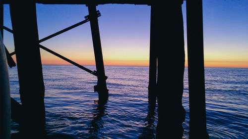 Silhouette wooden posts in sea against orange sky