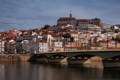 Bridge over river by buildings in town against sky