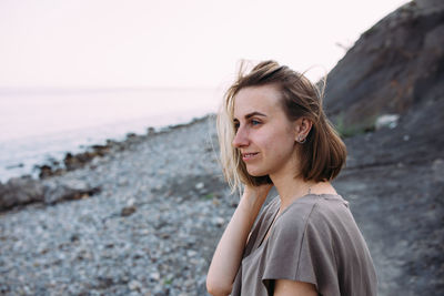 Beautiful relaxed young woman sits on a stone near the sea.