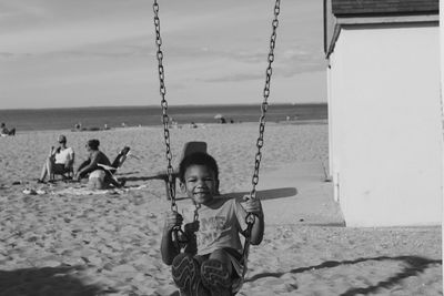 Portrait of smiling boy sitting on swing at beach