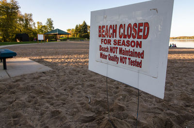 Information sign on sand at beach against sky