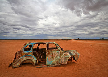 Damaged car on field against cloudy sky at dusk