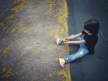 High angle view of girl holding yellow flowers while sitting on footpath