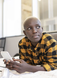 Short haired woman looking away while using phone on bed at home