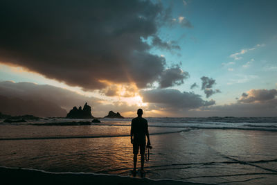 Silhouette man standing on beach against sky during sunset