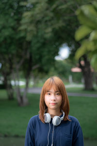 Portrait of young woman with headphones standing in park