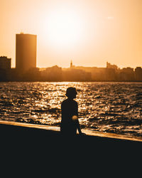 Rear view of silhouette woman standing at beach against sky during sunset