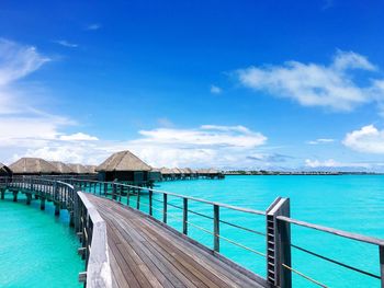 Pier by bungalows on lagoon against sky at bora bora island