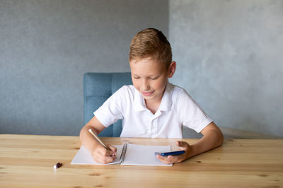 Cute boy writes in an open notebook and looks at the phone.