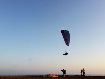 Paraglider paragliding over people on cliff against sky during sunset