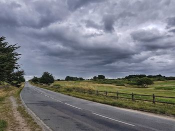Road by field against storm clouds