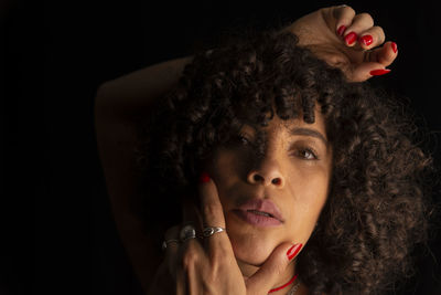 Close-up portrait of a woman with her hands on her face and head against black background. 