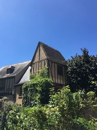 Low angle view of trees and building against clear blue sky