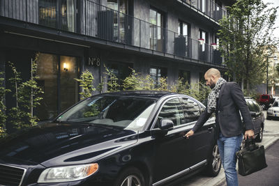 Mid adult businessman holding briefcase while opening car door