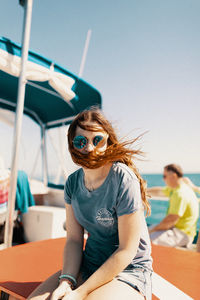 Young woman sitting on sunglasses against sky