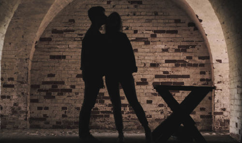 Rear view of silhouette couple standing against brick wall