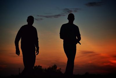 Silhouette men against orange sky during sunset