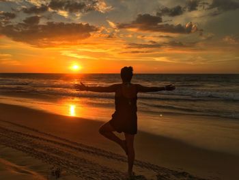 Rear view of woman exercising on shore at beach