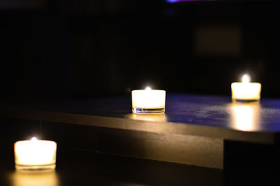 Lit tea light candles on table in darkroom