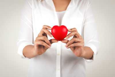 Midsection of woman holding heart shape over white background