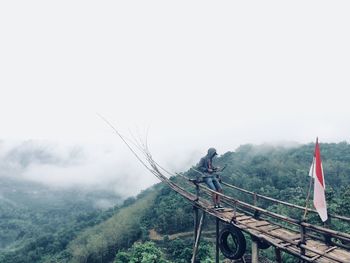 Man standing on wooden jetty over mountain against sky