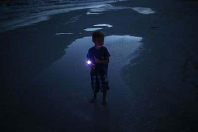High angle view of boy holding flashlight while standing at beach