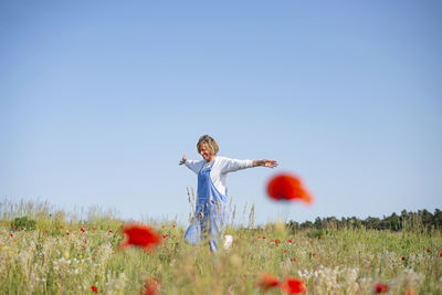 Rear view of woman with arms raised standing on field against clear sky