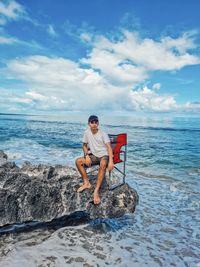 Full length of boy on rock at beach against sky