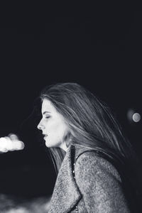 Portrait of young woman looking away against black background