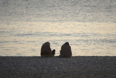 Women sitting at beach against sea during sunset