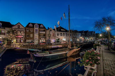 Boats moored at illuminated city against sky at night