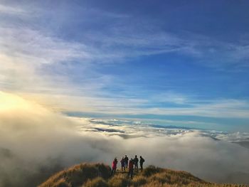 People on mountain against cloudy sky during sunset