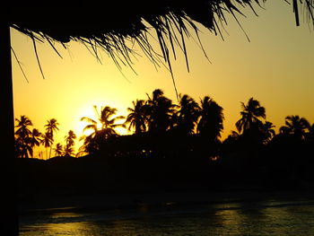 Silhouette palm trees by sea against sky during sunset