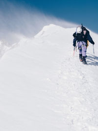 Low angle view of hiker walking on snowcapped mountain against sky